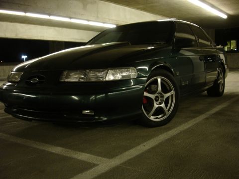 1993 Ford Taurus - Dark green 1993 Ford Taurus parked in a dimly lit parking garage with aftermarket wheels.