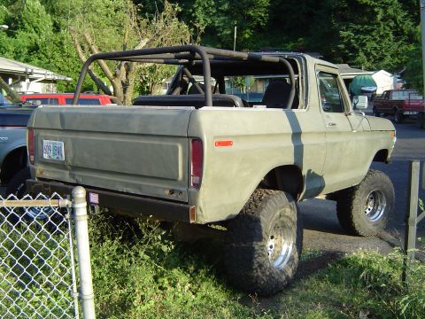 1978 Ford Bronco - Olive green 1978 Ford Bronco with roll cage and lifted suspension is parked outdoors.