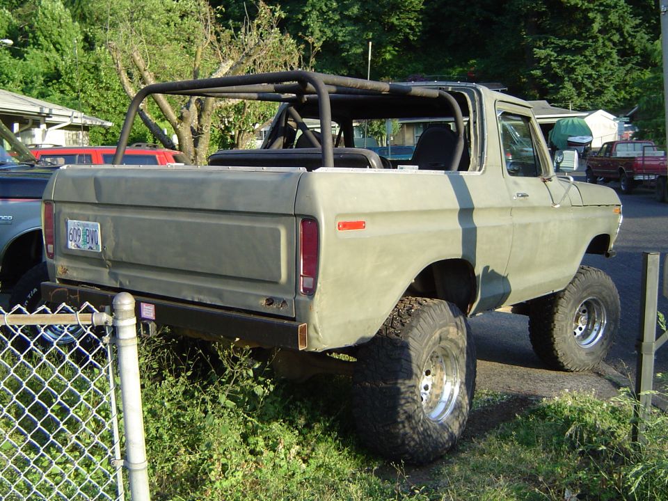 Olive green 1978 Ford Bronco with roll cage, lifted suspension, and aftermarket wheels, viewed from the rear