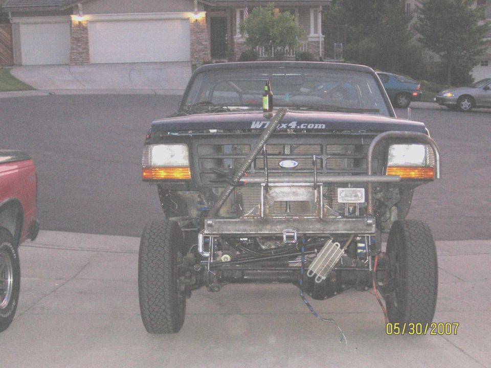 Dark blue Ford 4x4 in driveway with front end stripped showing tube bumper and radiator