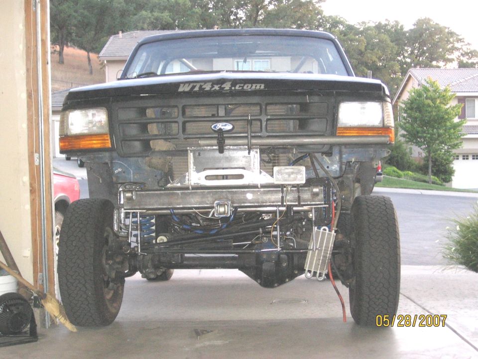 Black Ford 4x4 front end stripped to the frame in a driveway, WT4x4.com hood decal, on jack stands