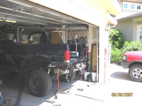 1994 Ford Bronco - A black SUV, possibly undergoing modifications, is parked inside a garage with a roll cage visible.