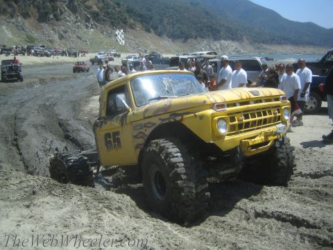 1987 Suzuki Samurai - A heavily modified yellow pickup truck navigates a muddy terrain with spectators watching nearby.