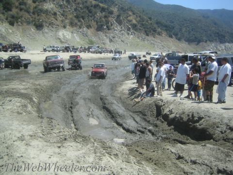 1987 Suzuki Samurai - Multiple off-road vehicles navigate a challenging muddy track with onlookers observing the action.