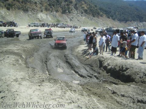 1987 Suzuki Samurai - A red 1987 Suzuki Samurai navigates a muddy off-road course with spectators watching.
