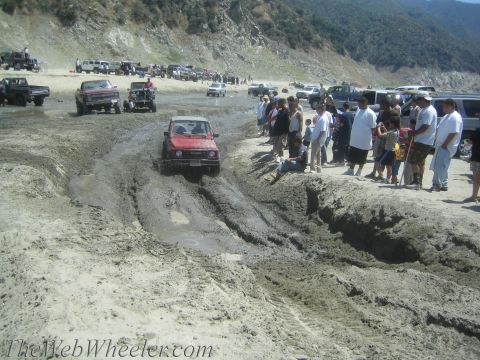 1987 Suzuki Samurai - A group of people watch as a red Suzuki Samurai navigates a challenging muddy terrain.