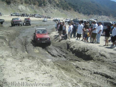 1987 Suzuki Samurai - A red 1987 Suzuki Samurai navigates a muddy track with spectators watching from the side.