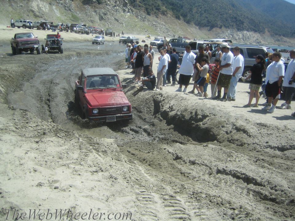 Red 1987 Suzuki Samurai navigating a muddy off-road course with spectators watching