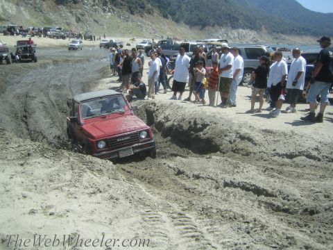 1987 Suzuki Samurai - Red 1987 Suzuki Samurai stuck in mud pit with crowd observing.