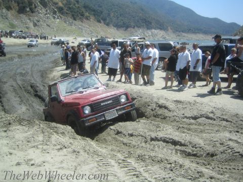1987 Suzuki Samurai - A group of people watch as a red Suzuki Samurai gets stuck in the mud near a body of water.