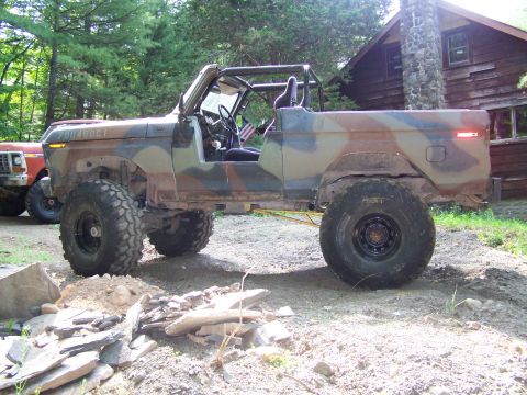 1979 Ford Bronco - Modified 1979 Ford Bronco with camouflage paint and off-road tires sits outside a wooden cabin.