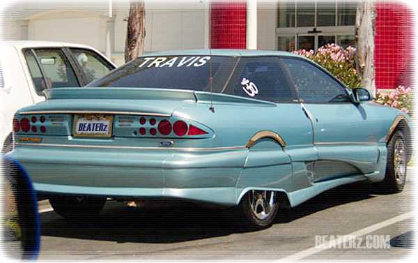 Teal Ford Probe with body kit, rear wing, TRAVIS window banner, and BEATERz plate, seen from rear three-quarter