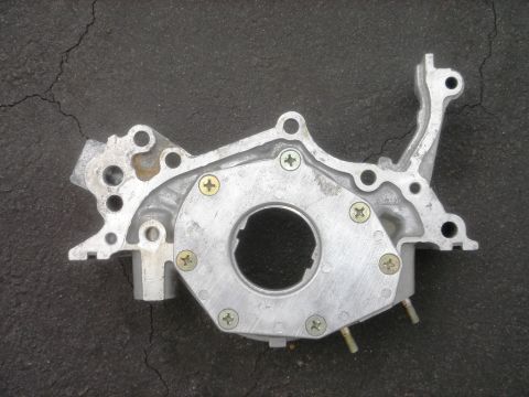 1991 Ford Taurus - This aluminum oil pump features a central circular opening and several mounting points, with visible screws securing its components.