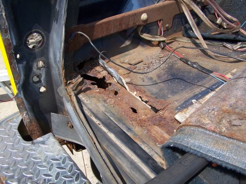 1986 Ford Bronco - Severe rust damage in the floor pan and rocker area of a dark blue truck with the carpet and seats stripped out, showing rust-through holes…