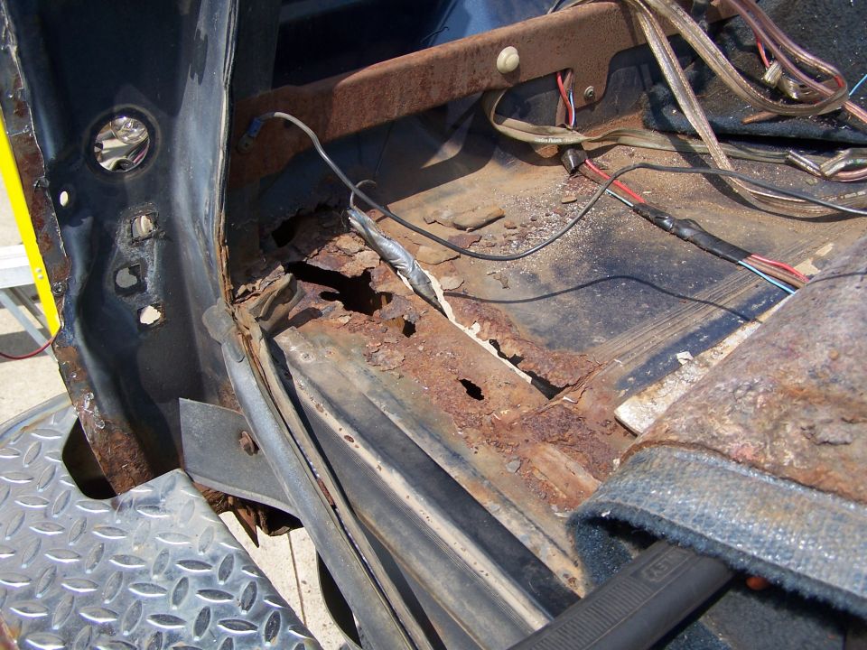 Rusted-through floor pan and rocker at the door opening with carpet removed