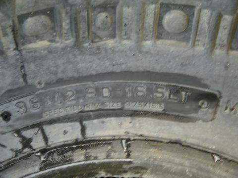 1988 Ford Bronco - Tight close-up of a dusty off-road tire sidewall, with molded lettering reading "36x12.50-16.5LT" and beneath it "SPECIFIED RIM SIZE 9.75x1…