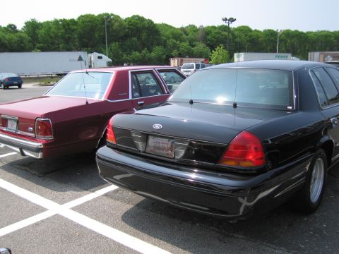 1991 Ford LTD Crown Victoria - Two Ford Crown Victorias, one black and one maroon, are parked in a lot.