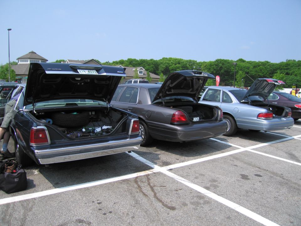 Dark blue Ford Crown Victoria with trunk open, showing spare tire and contents