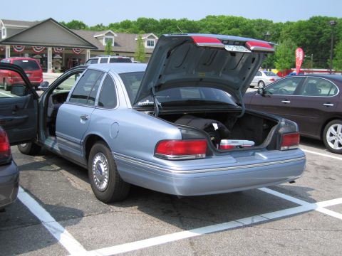 1991 Ford LTD Crown Victoria - A light blue 1991 Ford Crown Victoria LTD is parked with its trunk and driver door open, revealing items inside.