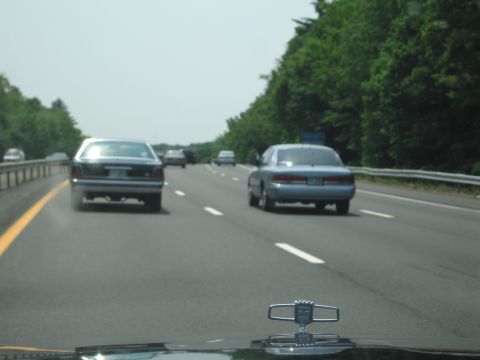 1991 Ford LTD Crown Victoria - Several cars travel down a highway on a clear day, with trees lining the right side of the road.