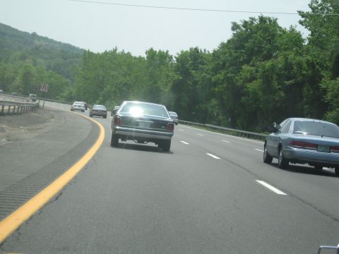 1991 Ford LTD Crown Victoria - A dark sedan drives on the highway, its rear reflecting the bright sun.