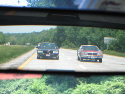 1991 Ford LTD Crown Victoria - Two cars are seen on a highway, viewed through a rearview mirror.