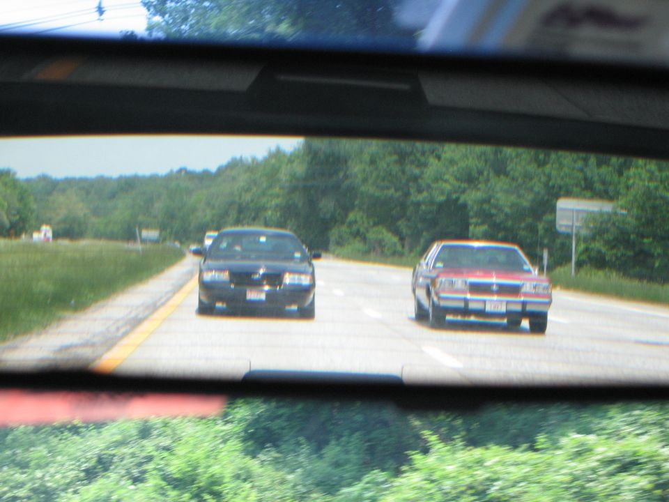 View from rearview mirror shows a black car and a red car driving on a highway