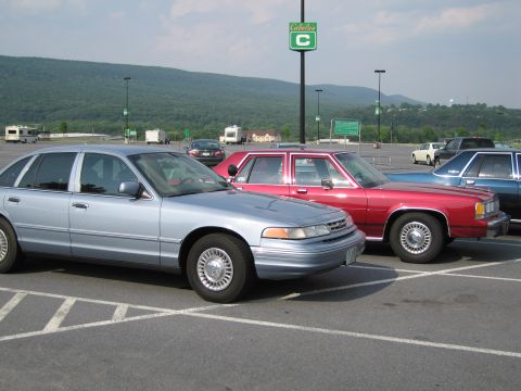 1991 Ford LTD Crown Victoria - A light blue sedan is parked in a lot next to a red sedan, with mountains in the background.