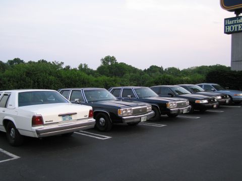 1991 Ford LTD Crown Victoria - Several Ford Crown Victoria police cars are parked in a lot next to a hotel.