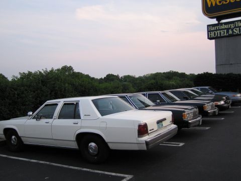1991 Ford LTD Crown Victoria - Several cars are parked in a lot next to a hotel and restaurant.
