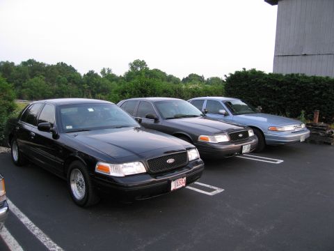 1991 Ford LTD Crown Victoria - Three Ford Crown Victoria sedans are parked in a lot. The black car in front is a 1991 model.