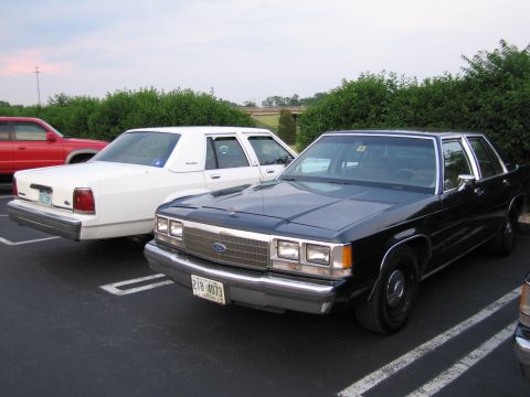 1991 Ford LTD Crown Victoria - Two sedans are parked in a lot, with a red SUV partially visible on the left.