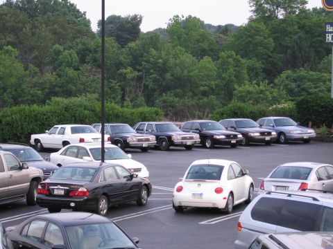 1991 Ford LTD Crown Victoria - A variety of vehicles are parked in an outdoor lot, with trees and a building visible in the background.