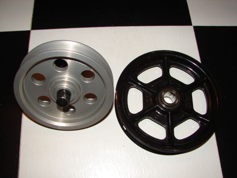 1992 Ford Taurus - Two pulleys are shown on a checkered surface. One pulley is silver with multiple grooves, and the other is black with a bearing.