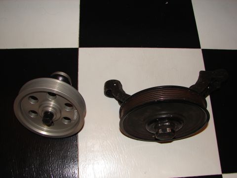 1992 Ford Taurus - Two automotive pulleys are displayed on a checkered floor, one silver and one black with a mounting bracket.