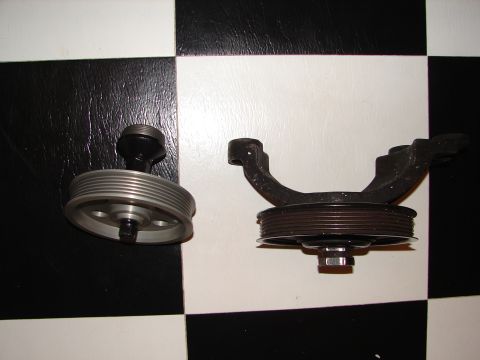 1992 Ford Taurus - Two automotive pulleys and a mounting bracket are displayed on a black and white checkered surface.