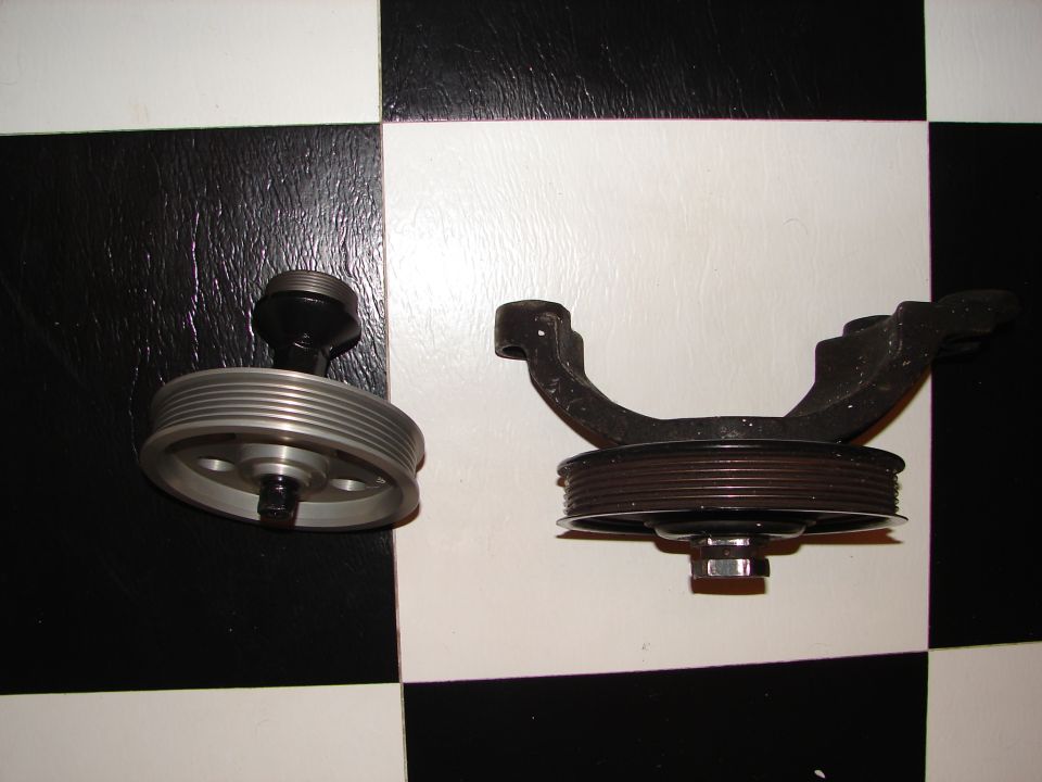Clean aluminum serpentine pulley bracket next to a rusty used one on a checkered floor