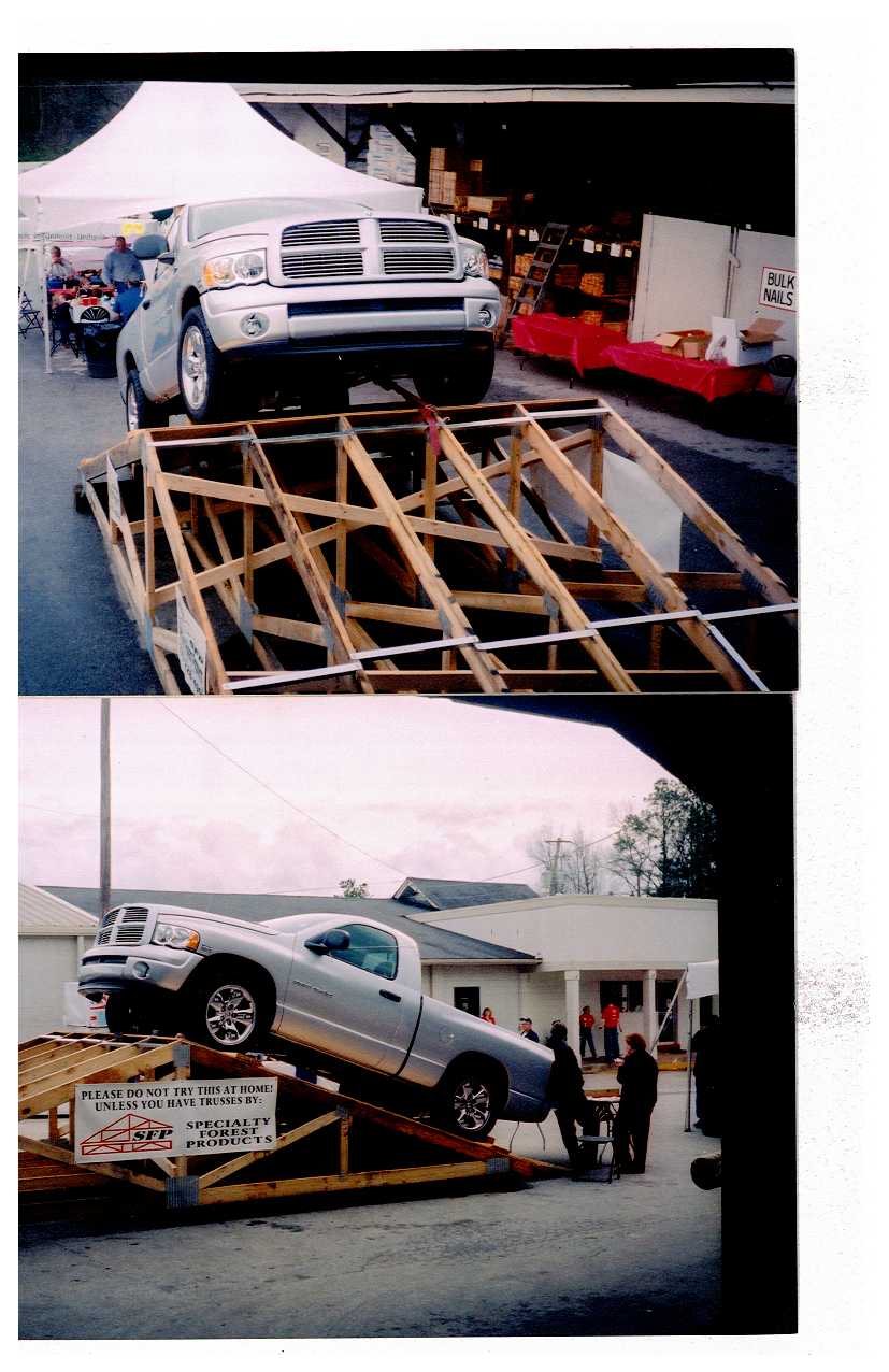 Silver Dodge Ram pickup truck on wooden ramps, with a sign that says 'PLEASE DO NOT TRY THIS AT HOME. UNLESS YOU HAVE TRUSSES BY SFP SPECIALTY FOREST PRODUCTS.'