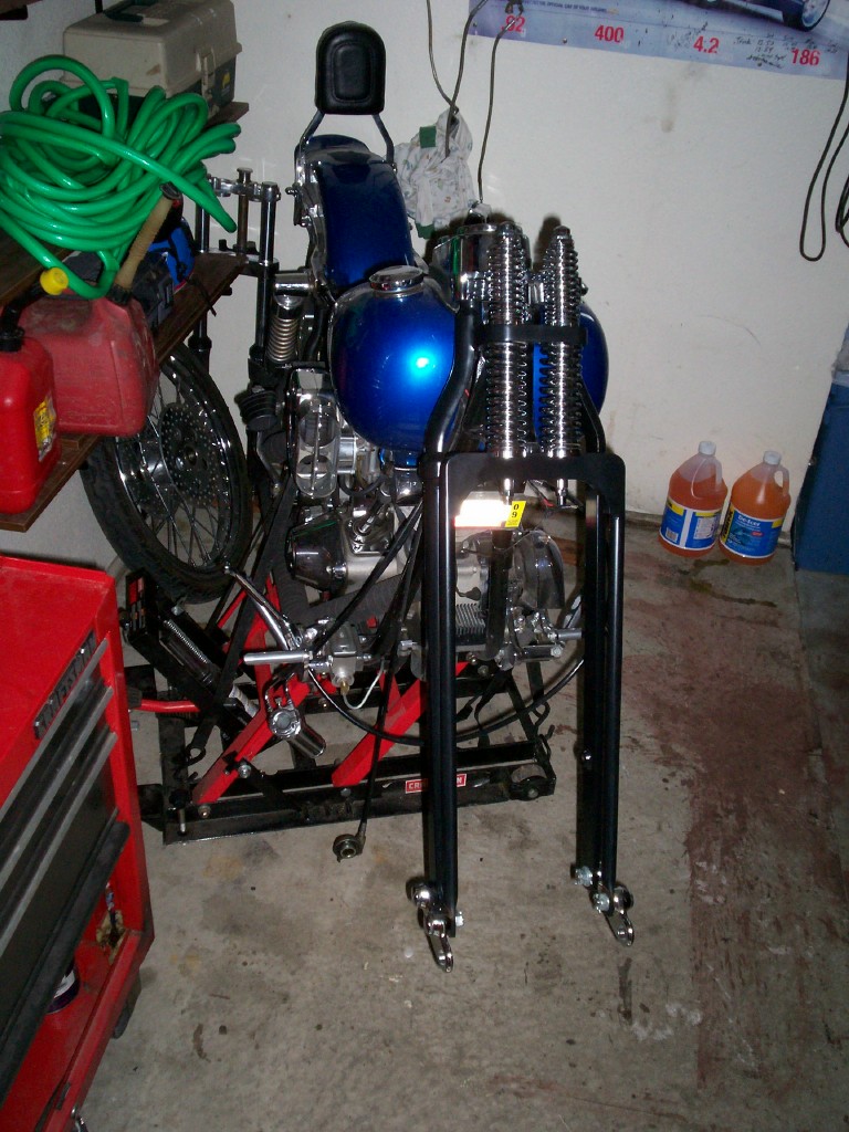 Partially built motorcycle with blue tank on a lift in a garage
