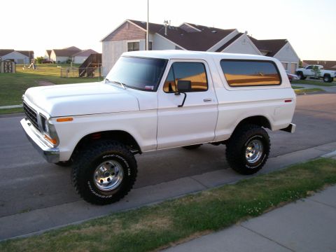 1979 Ford Bronco - This lifted Ford Bronco sits on a residential street with houses and a lawn visible.