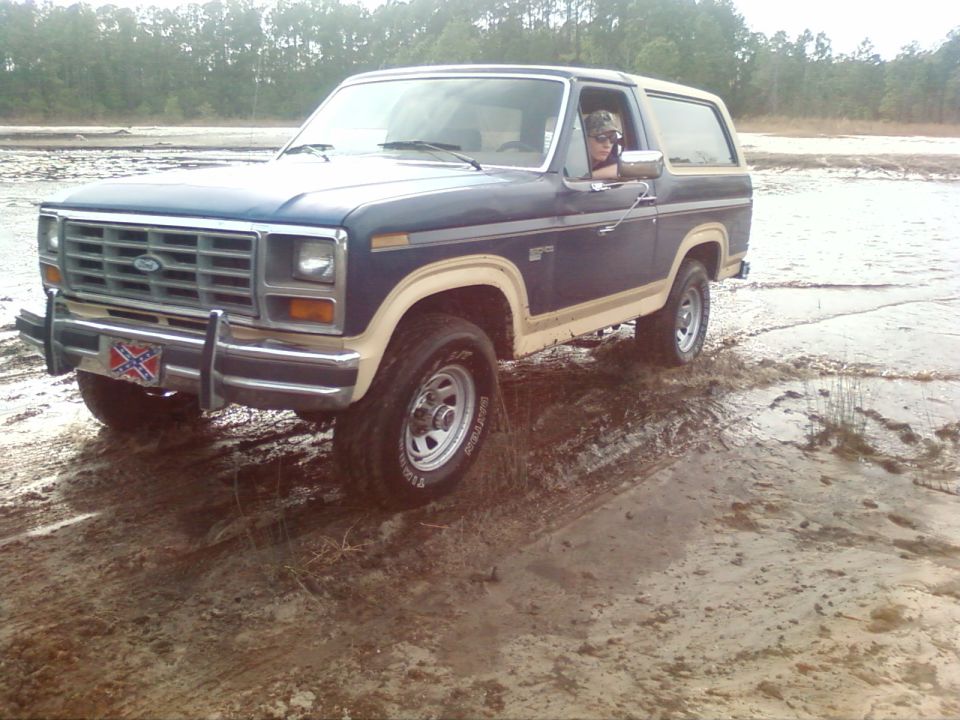 Blue Ford Bronco with tan trim driving off-road in muddy terrain