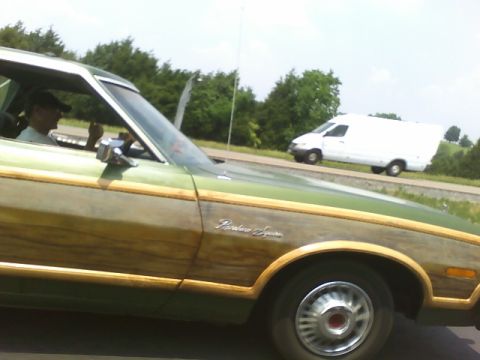 1972 Ford Ranchero - A green Ford Ranchero Squire with wood paneling is seen on the road next to a white van.