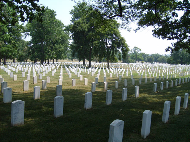 Rows of white headstones in a cemetery under a bright sky