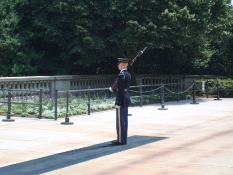 2004 Ford Crown Victoria - A soldier stands guard at attention in front of a memorial site, with trees and a stone balustrade in the background.