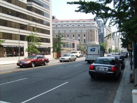 2004 Ford Crown Victoria - A red sedan and a black sedan are parked on a city street next to buildings and trees.