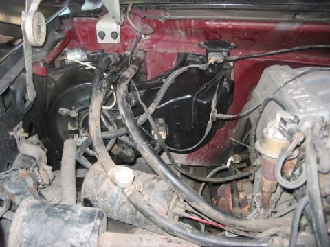 1991 Ford Bronco - Close-up view of engine bay components, including hoses and wiring, against a red firewall.