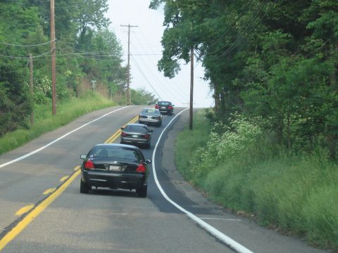 1991 Ford LTD Crown Victoria - A line of cars travels down a rural road on a cloudy day.