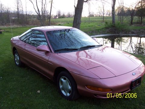 1996 Ford Probe - A pink 1996 Ford Probe is shown from a 3/4 front angle, parked on a grassy area next to a body of water.