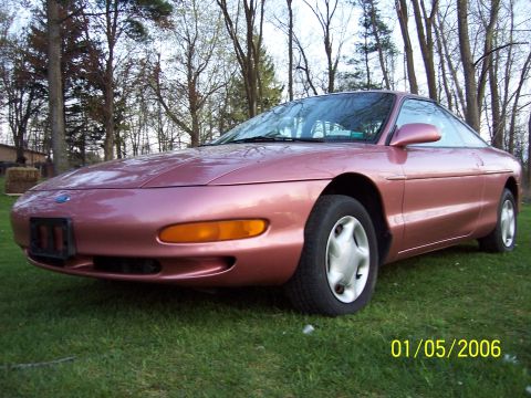 1996 Ford Probe - This pink coupe is viewed from the front 3/4 angle, parked on a grassy lawn with trees in the background. A date stamp is visible in the lo…