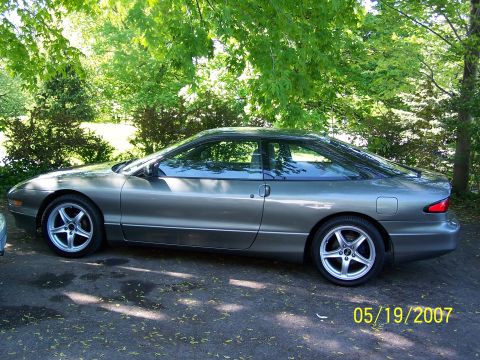 1996 Ford Probe - A gray 1996 Ford Probe is shown from the side, parked on an asphalt surface with trees in the background.